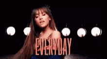ariana grande is standing in front of a sign that says `` everyday '' in a dark room .
