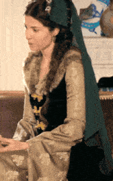 a woman wearing a black and gold dress with a fur collar sits on a couch