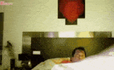a man is laying on a bed in a bedroom with a red heart on the wall behind him