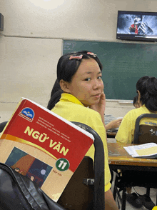 a girl sitting in a classroom with a book titled ngữ văn