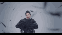 a woman in a black dress and crown is standing in front of a flock of birds flying around her .
