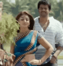 a woman in a blue saree is standing next to a man in a striped shirt .