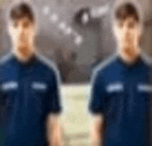 a blurry picture of two men standing next to each other in blue shirts .