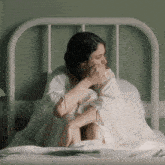 a woman in a white dress is sitting on a bed with her knees crossed .
