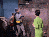 a man in a batman costume stands in front of a woman in a green dress