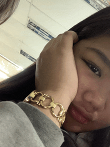 a woman wearing a gold watch has her hand on her forehead
