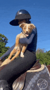 a woman wearing a helmet holds a puppy on her lap while riding a horse