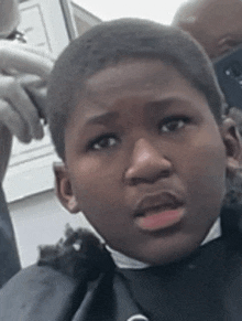 a young boy is getting his hair cut by a barber while wearing a black cape .