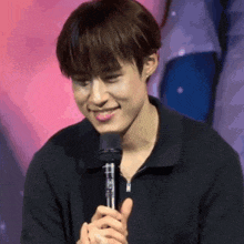 a young man is smiling while holding a microphone in his hands .
