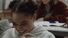 a young girl is laughing in a classroom while sitting at a desk with other students .