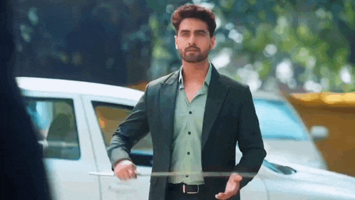 a man in a suit is standing in front of a car .