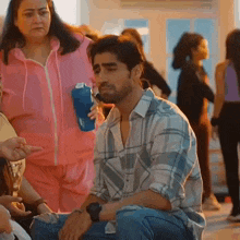 a man in a plaid shirt is kneeling down while a woman in a pink jacket holds a blue water bottle