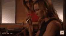 two women are sitting at a table with arrow written on the bottom of the screen