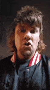 a man with a mullet is wearing a blue jacket with red and white stripes