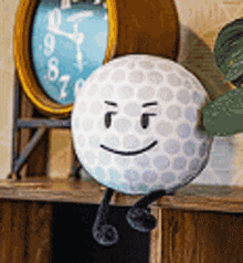 a stuffed golf ball with arms and legs is sitting on a shelf next to a clock .