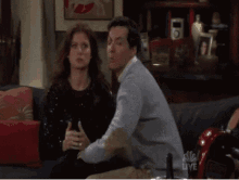 a man in a grey sweater is sitting on a couch with a woman behind him .