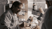 a man in a lab coat is eating a sandwich while another man watches