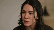 a woman with long black hair looks at the camera