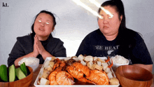 two women are sitting at a table with a plate of food and one of them is wearing a shirt that says " the beat "
