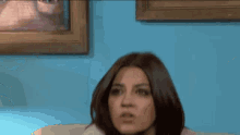 a woman is sitting in front of a blue wall with a framed picture on it