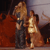 a woman is singing into a microphone while a little girl in a gold dress stands behind her