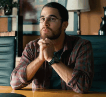 a man wearing glasses and a watch sits at a table with his hands folded