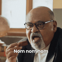 a man with glasses and a beard is eating a cookie with the words nom nom nom behind him