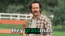 a man with a mustache is standing in front of a fence and says hey grassman