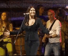 a woman singing into a microphone with a man playing a guitar behind her