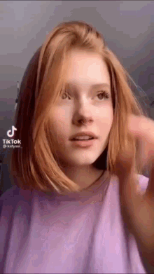a woman with red hair and a nose ring is wearing a purple shirt and making a funny face .