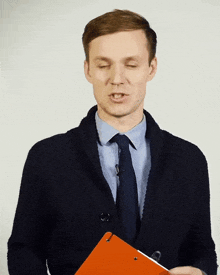 a man in a black jacket and tie is holding an orange clipboard