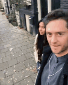 a man and a woman are standing on a sidewalk looking at the camera