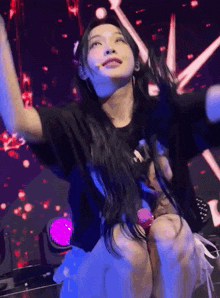 a woman is sitting on a stage with her arms outstretched and a microphone in her hand .