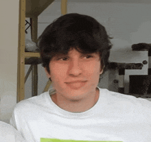 a young man wearing a white t-shirt is smiling in front of a cat tower