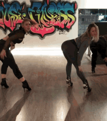 two women are dancing in front of a wall with graffiti on it that says ' us girls '