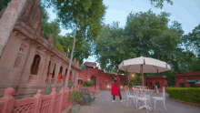 a woman in a red dress stands in front of a table and chairs under an umbrella