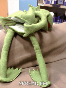 a stuffed kermit the frog is laying on a couch with the words spread em written below it