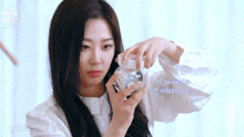 a woman in a white shirt is holding a glass bottle with a foreign language written on it