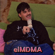 a man is sitting on a couch with a microphone in his hand and the word eimdma written on the screen
