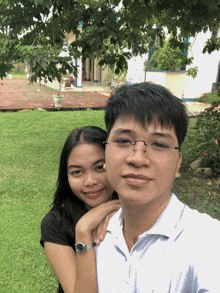 a man and a woman pose for a picture in front of a tree