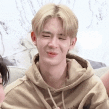 a young man in a tan hoodie is making a funny face .