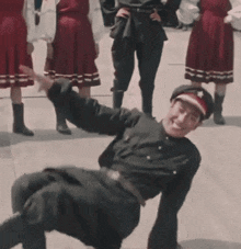 a man in a black uniform is doing a handstand in front of a group of people in red dresses .