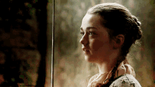 a young girl is holding a sword in her hand and looking out of a window .