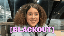 a woman with curly hair is smiling in front of a sign that says " blackout "