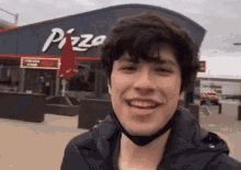 a man wearing a mask is smiling in front of a pizza hut restaurant .
