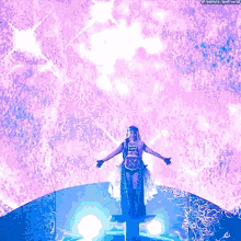 a woman is standing on a stage with her arms outstretched in front of a pink background .