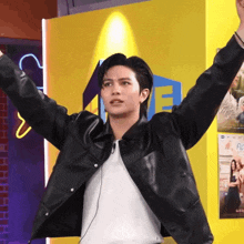 a man in a black jacket is standing with his arms outstretched in front of a sign that says ' a '