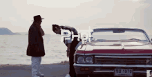 two men are standing next to a red car that has a license plate that says 1970