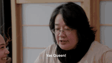 a woman wearing glasses says yas queen in front of a window