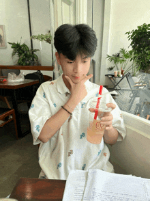 a young man sitting at a table holding a cup with a straw that says coffee on it